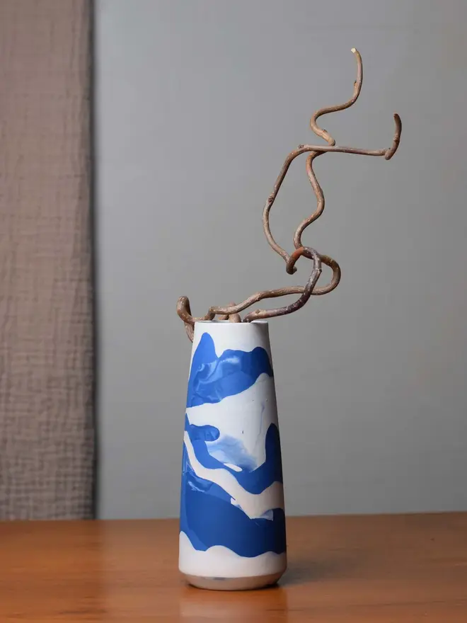 vase on wooden table, vase has streaky pattern in shades of blue and holds dry plant