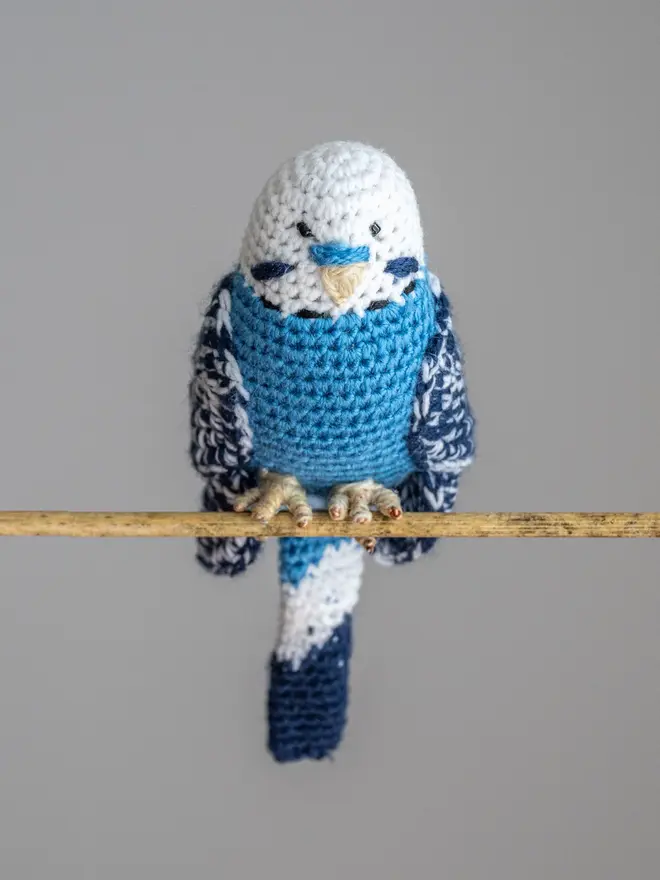 Budgerigar Hand Crocheted Figure, a blue  crocheted bird sitting on a wooden poll. 