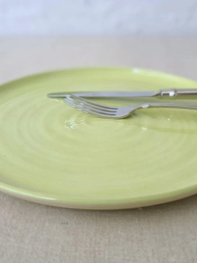 Classic Ceramic Dinner Plate, a colourful ceramic dinner plate sitting on a plain surface. It is accompanied by some cutlery. 