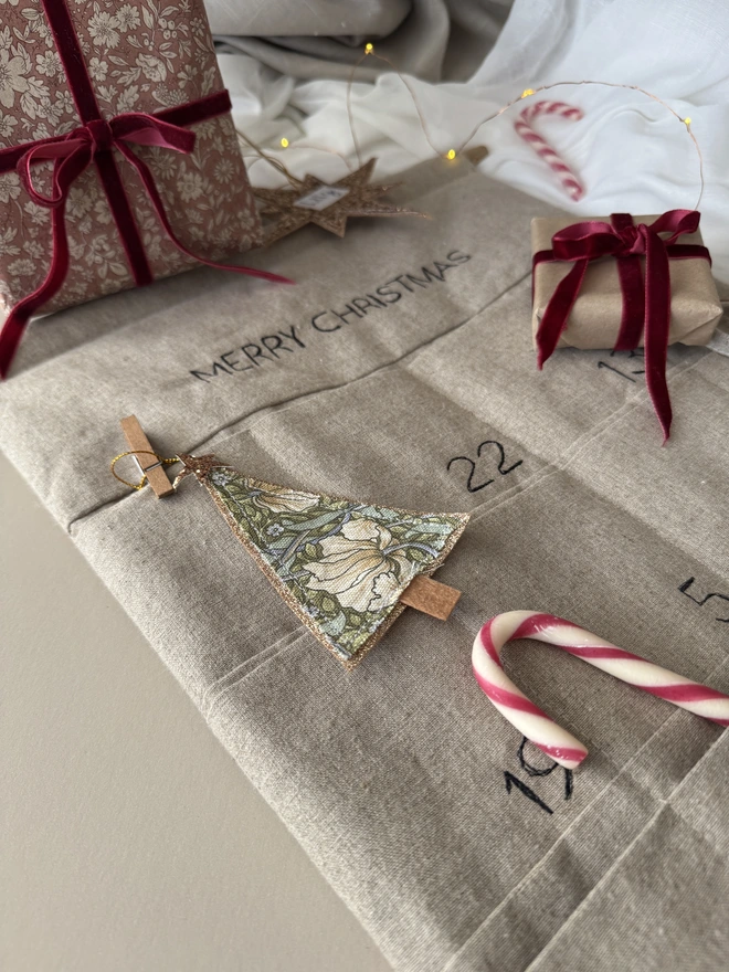 Linen advent calendar lay on a table with treats and gifts wrapped in red floral paper and velvet ribbon