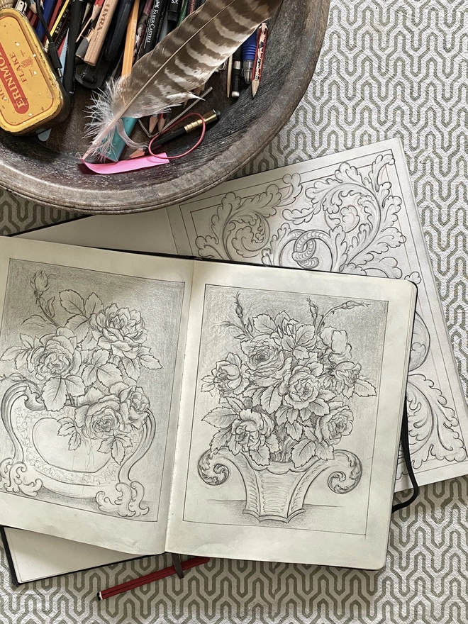 Sketchbook with pencil drawings of vases of flowers and a wooden bowl filled with drawing equipment