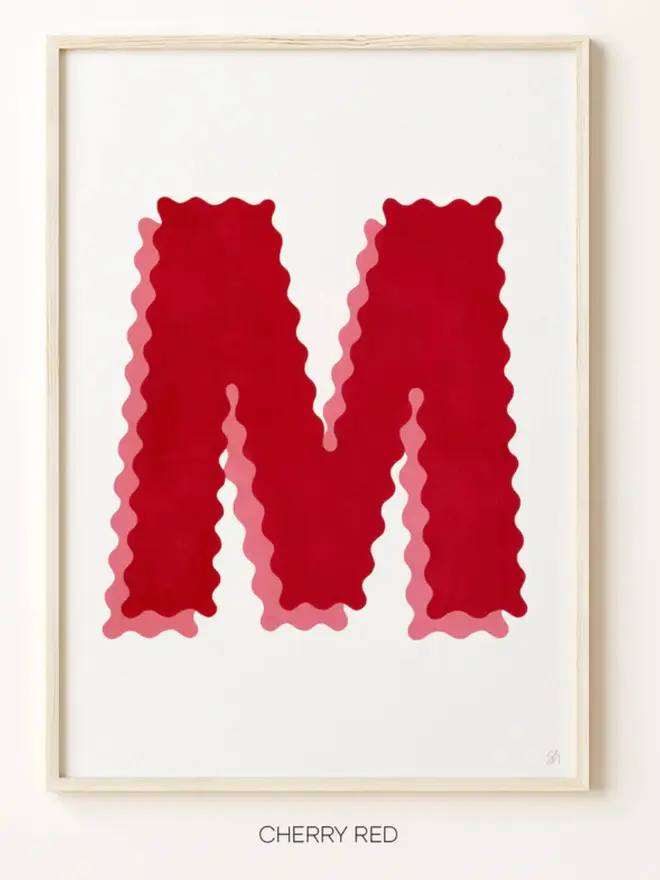 Framed wall art print featuring a large decorative letter “M” in red tones with a ric rac–style wavy edge design, centered on a white background. 