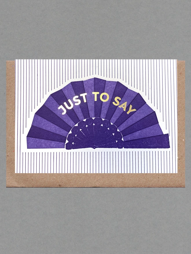 Purple and white striped card with a purple fan on it and gold text reading 'Just To Say' with a brown envelope behind