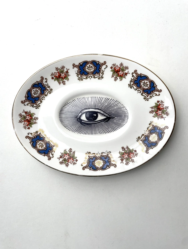 an ornate vintage plate with detailed patterned border, in the centre is printed an eye