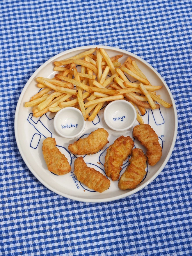 Dippy chips & Nuggets Dinner Plate, a white dip dinner plate with blue outlines for nuggets and chips, with real nuggets and chips on top. Sitting on a picnic cloth.