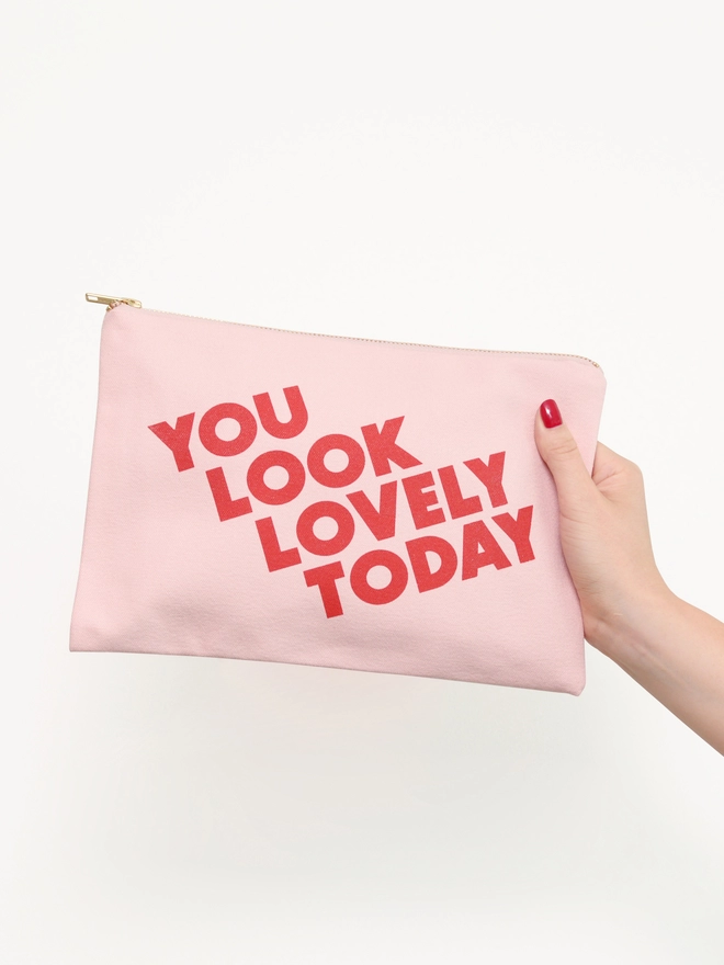 a hand holding out a blush pink canvas zip pouch with the words you look lovely today 