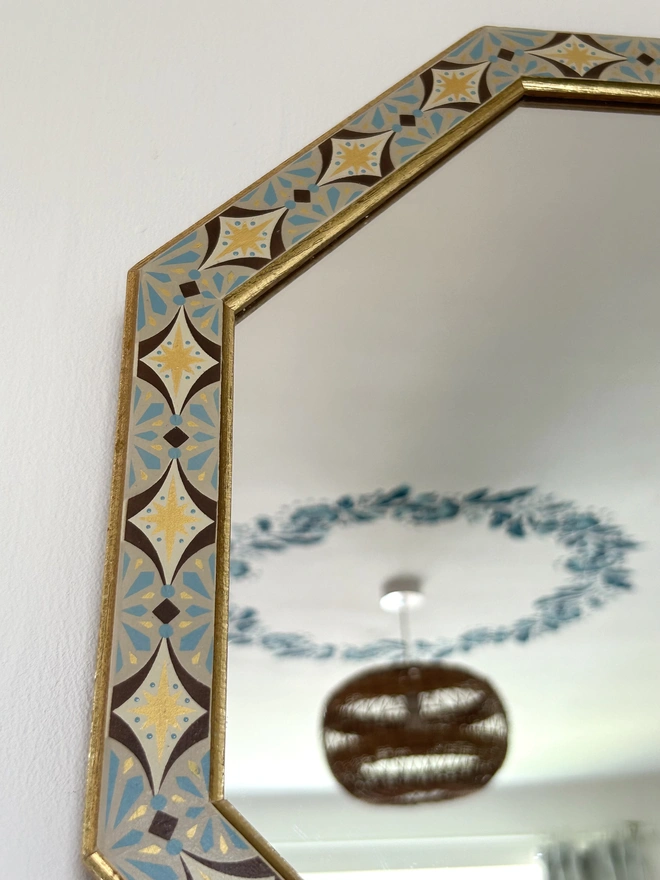 Medium sized octagonal wall mirror with a hand painted decorated frame with gold stars and blue star burst repeating pattern around the frame