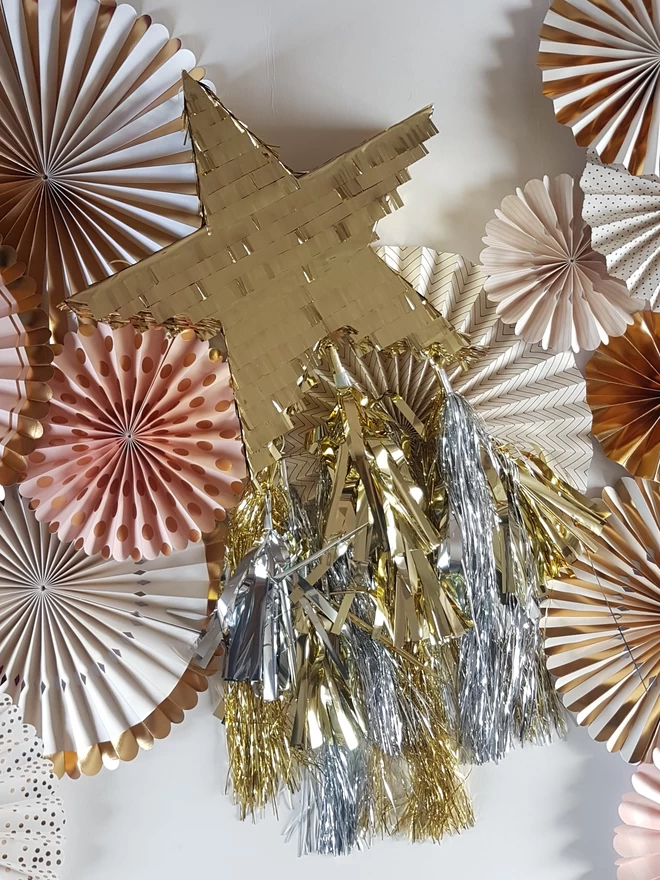 gold star pinata with silver and gold tassel tail on a paper fan background