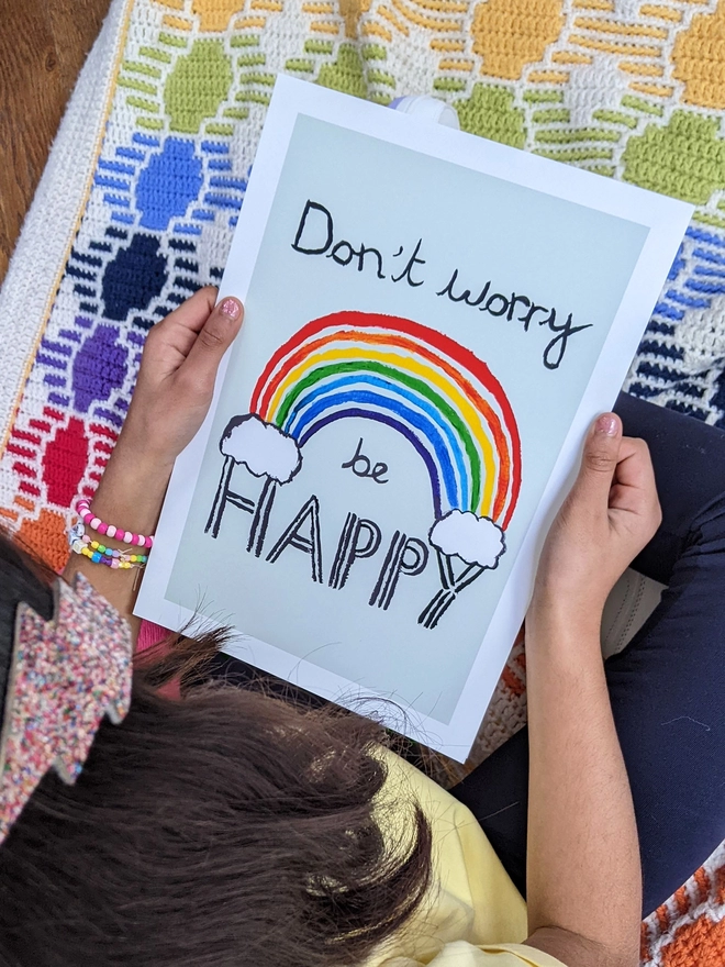 Young girl sitting holding an art print saying 'Don't worry be happy'