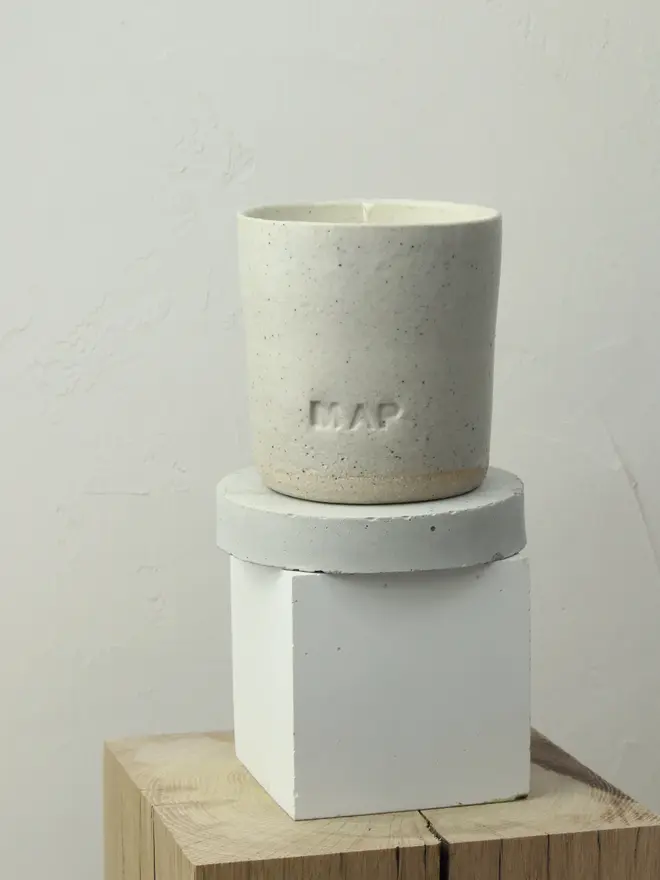 'St Helena' Soy Wax Candle And Ceramic Holder. candle in ceramic pot placed on top of white block.