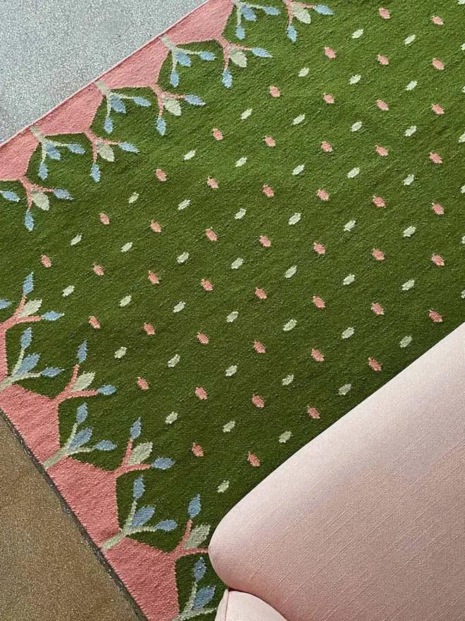 Hedgerow Flatweave Rug, a colourful rug sitting on a plain backdrop accompanied by some furniture. 