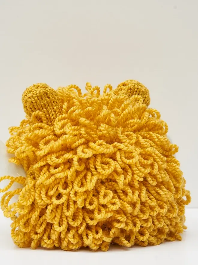 Lion Tea Pot Cosy Animal Lovers Tea Time Treat, a yellow lion tea pot cosy sitting on a tea pot, on a white surface against a grey backdrop. 