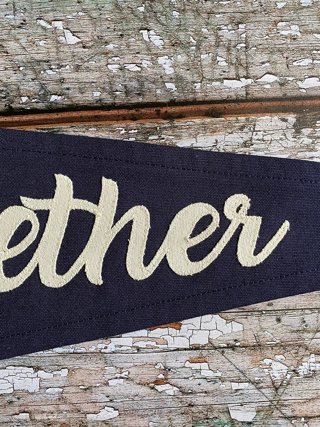 Detail of a navy 'Better Together' pennant flag. This shows the letters ther written in ivory canvas.