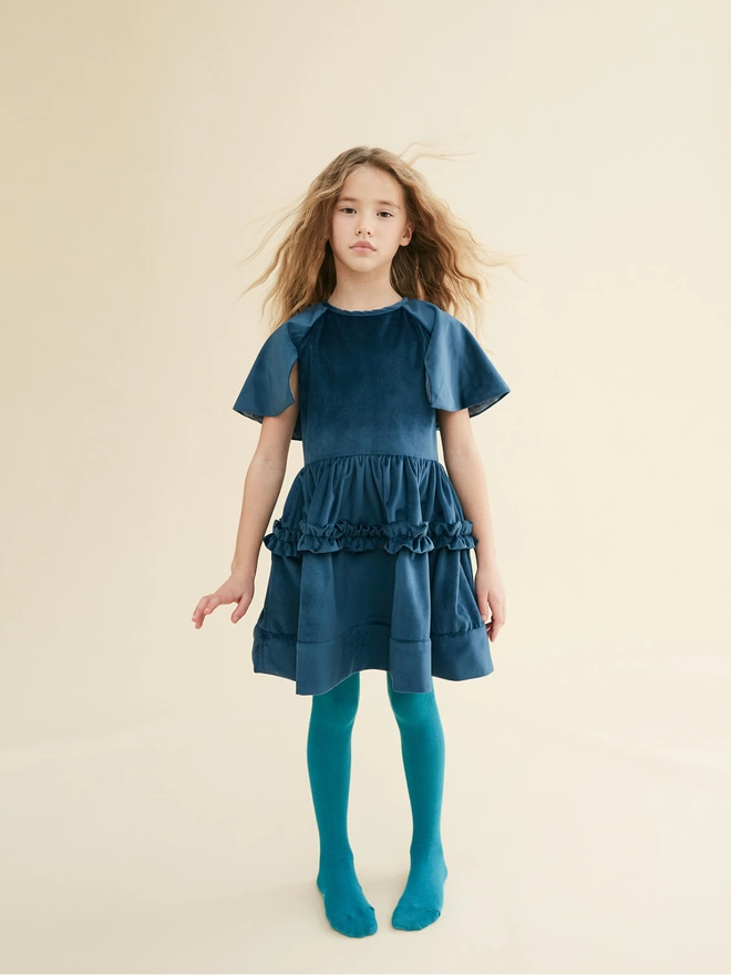 Dress made in a velvet with a fixed cape. Featuring laid on frills at hip and laid on hem for added shape. Concealed zip to centre back. Fully lined.