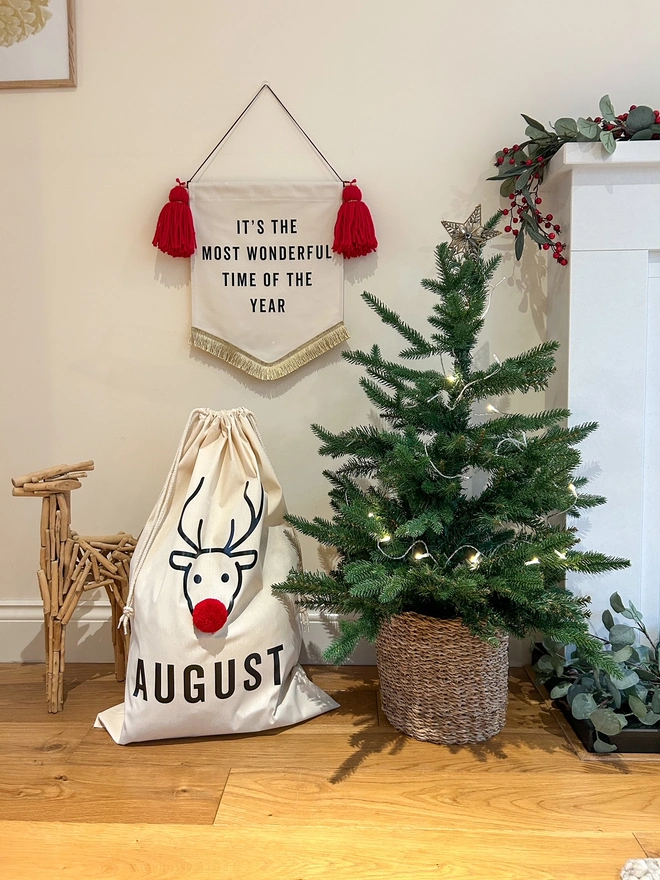 Reindeer Design Christmas Sack sitting beside a Christmas Tree. Reindeer design with pom pom nose