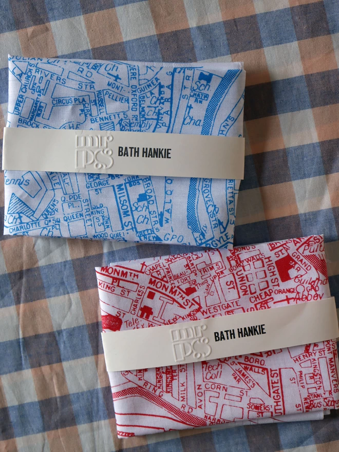 one sky blue and one red Mr.PS Bath Hankies shown folded with their packaging band