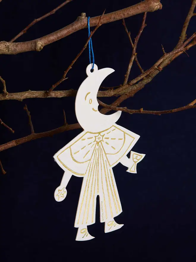 Decorative hanging ornament shaped like a stylized figure with a moon face, holding a glass, against a dark background.