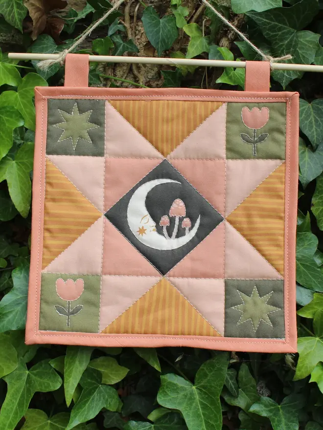 moon folk art quilt hanging. a patchwork hanging quilt with an embroidered moon in the centre.