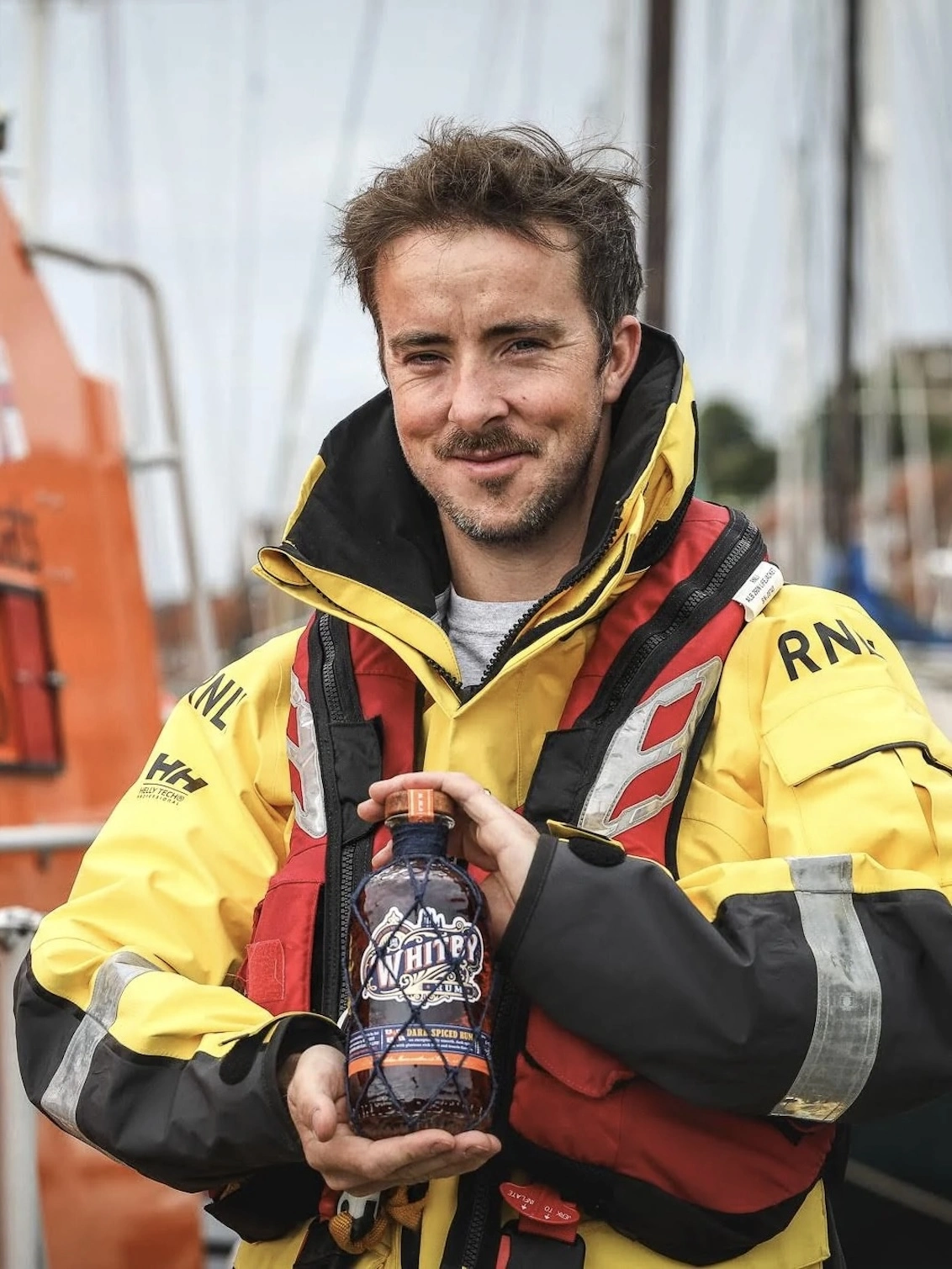 Whitby Dark Spiced Rum - RNLI Edition, a lifeguard holding a bottle of rum outside. 