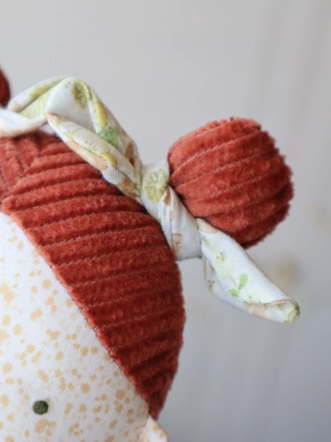 Close up of handmade heirloom cloth doll with freckled face, red corduroy hair in two buns, floral leggings, and a soft yellow dress.