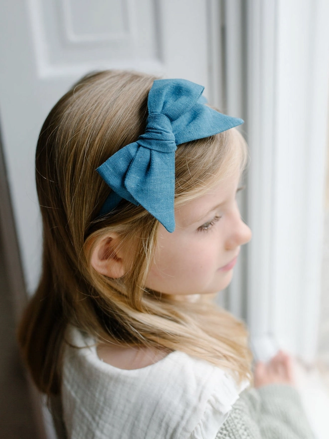 Little girl wearing a large bow on an Alice Band by window