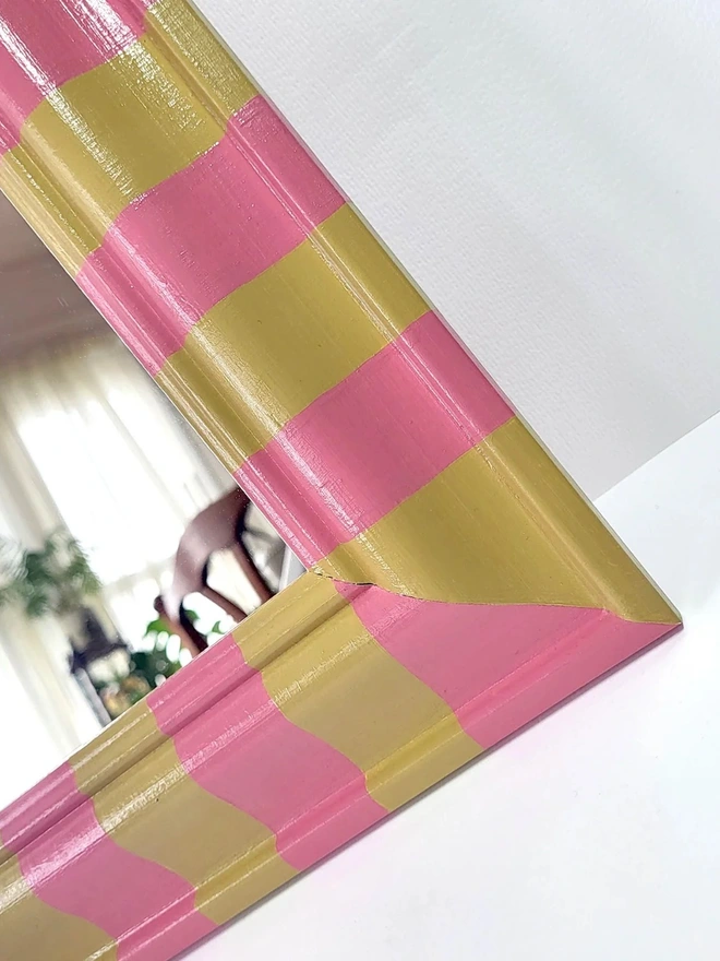 close up of wall mirror with bevelled wooden frame, painted in pink and yellow stripes