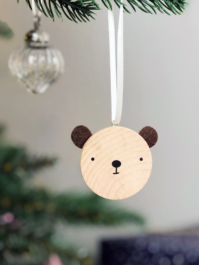 A small wooden and felt bear decoration hangs on a Christmas tree branch.