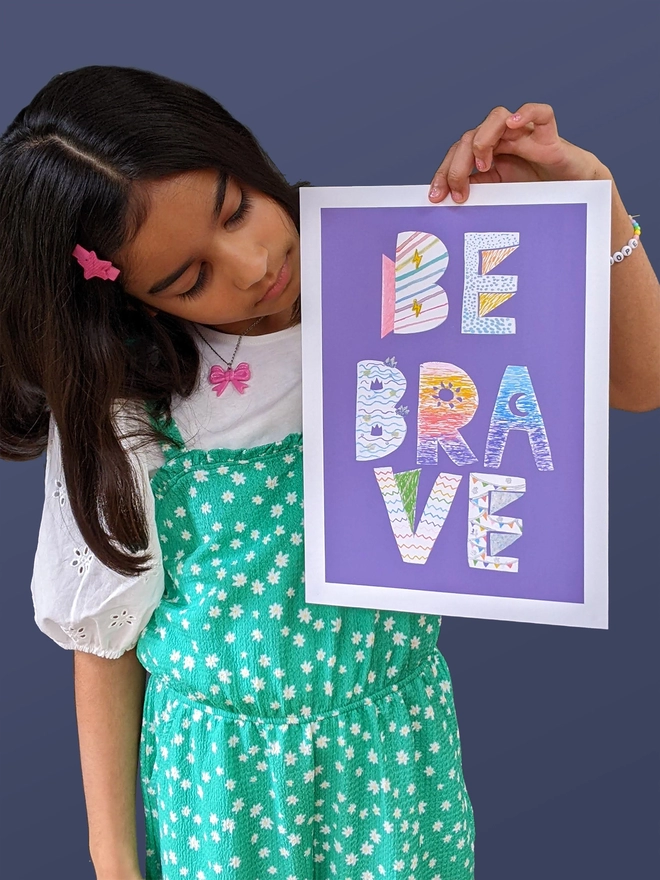 Young girl standing holding an art print saying 'Be brave'