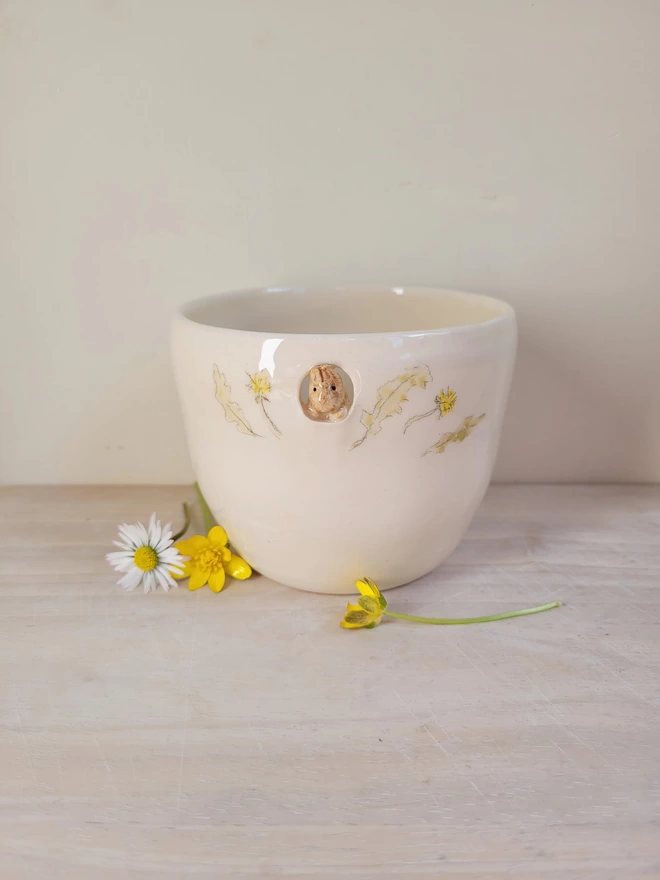 hand crafted pottery cacao cup with a tiny beige bunny rabbit peeking through a cut out circle near the rim with dandelions and leaves hand painted 