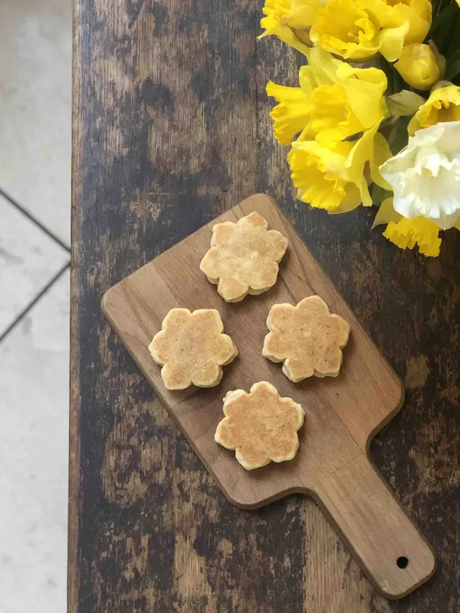 4 daffodil shaped welsh cakes on a wooden chopping board