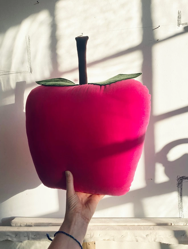 Large pink apple cushion held up by a window 