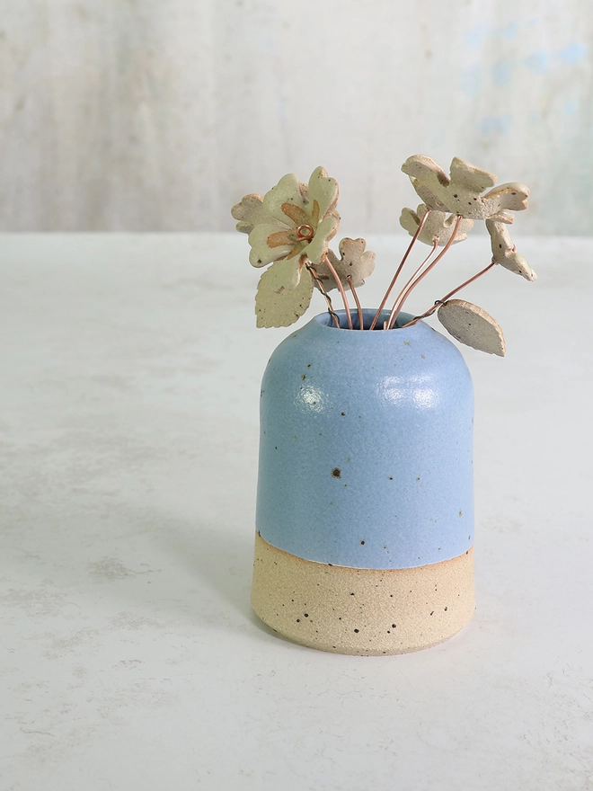 ceramic handmade flowers in a blue flecked clay vase on a white table top