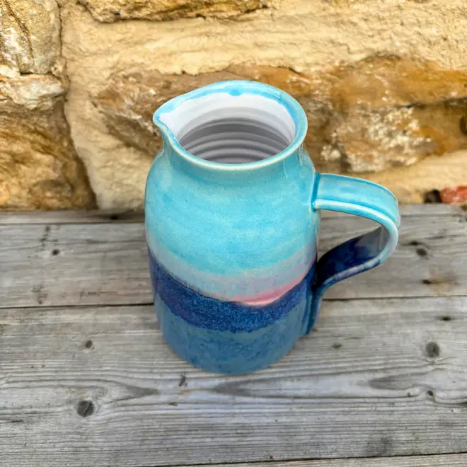 Landscape Medium Jug, a colourful jug sitting on a wooden surface against a brick backdrop. 
