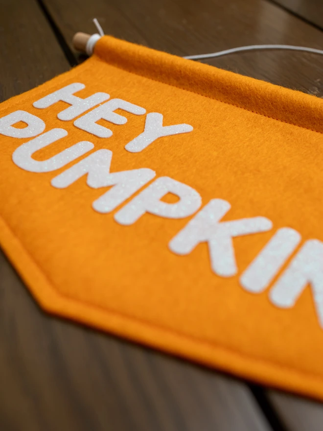 close up image of an orange, felt banner with the words "Hey Pumpkin" written on it in white glitter felt