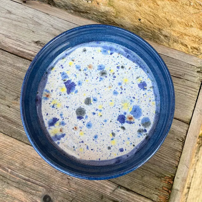 Shoreline Pasta Bowl, a colourful bowl placed on a wooden surface against a brick backdrop. 
