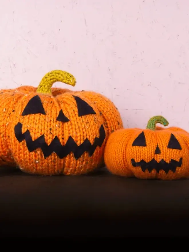 two knitted pumpkins, both with jack o lantern faces on table with black table cloth