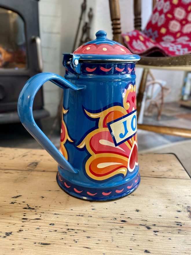 Blue vintage coffee pot, hand painted with a fairground inspired design in pink, orange and yellow. 'Joy' is painted in a banner through the centre of the design.