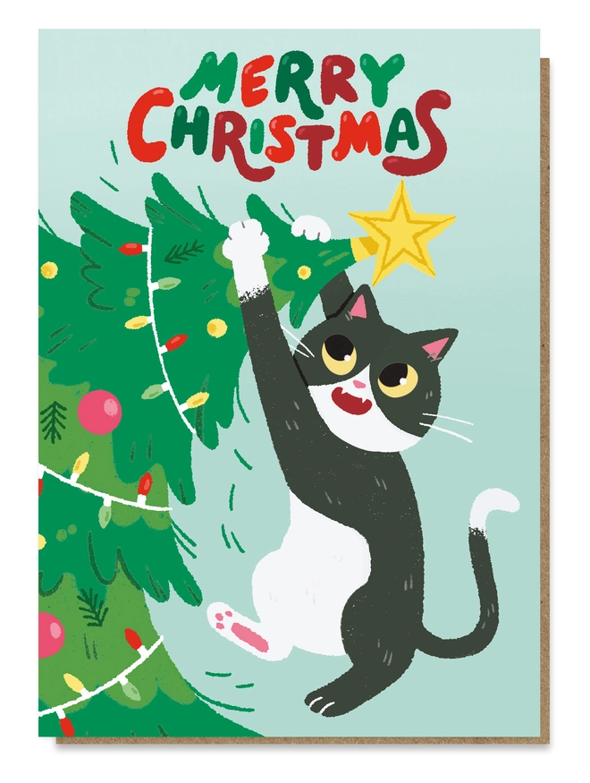 Black and white cat hanging from the top of a Christmas tree, topped with a star