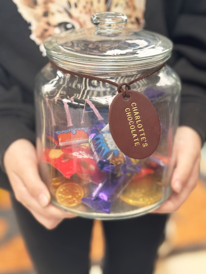 a glass jar with chocolate in, a leather label with 'charlotte's chocolates' stamped on the brown tag with gold writing.