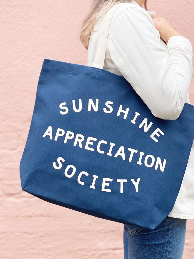 model carrying a large blue canvas tote bag with the words sunshine appreciation society on