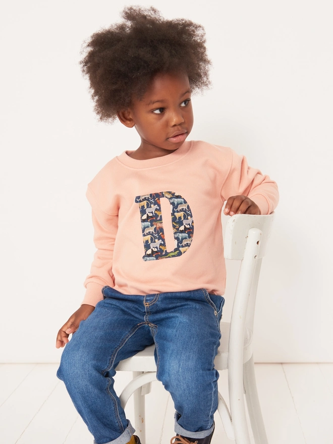 a 3 year old boy wearing a personalised dusty pink sweatshirt with his initial sewn on the front in zoo animal liberty print 