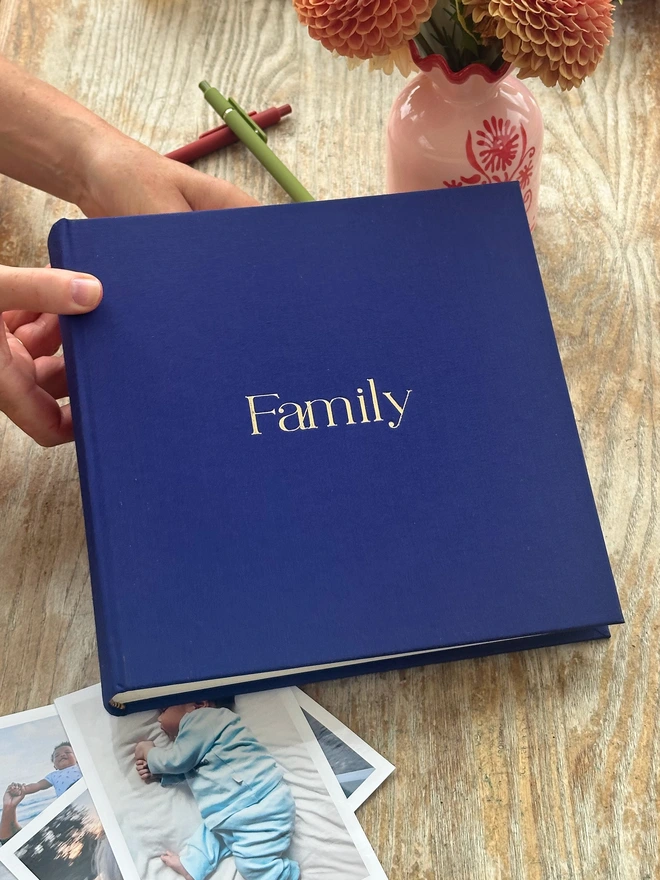 a woman is holding a blue photo album in her hands. It has been printed with the word Family on the front in large letters.