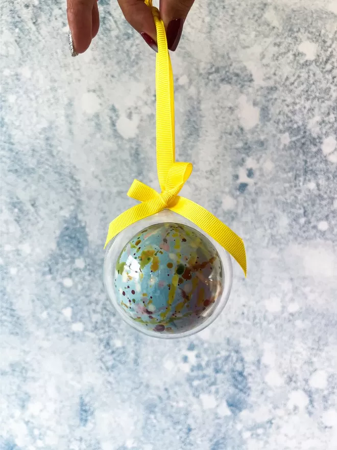 a hand holding a blue christmas ornament made out of chocolate with a yellow ribbon