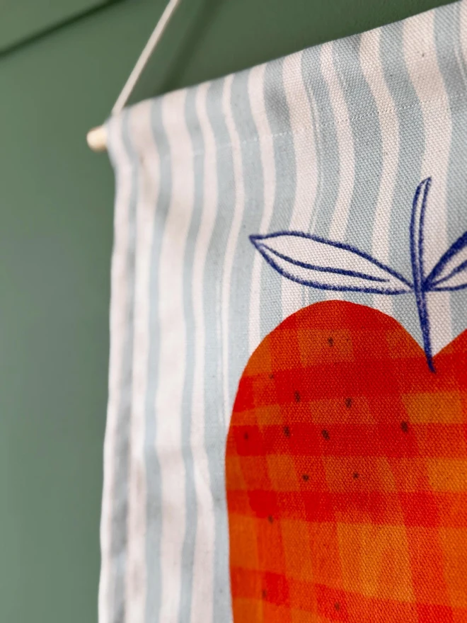 Cotton Apple Wall Hanging, against a green wall. 
