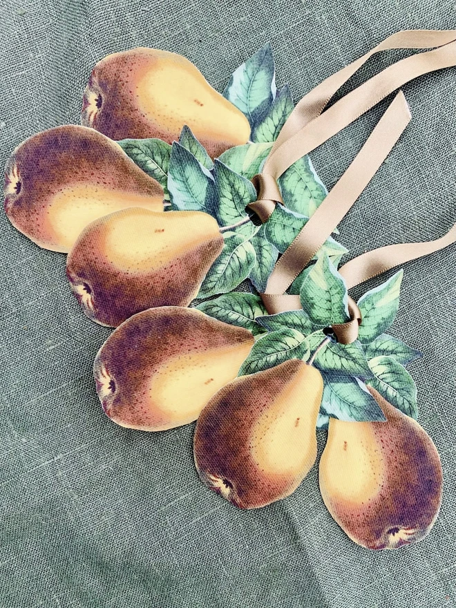 A set of six napkin ties with a botanical pear design, lying on a green linen tablecloth