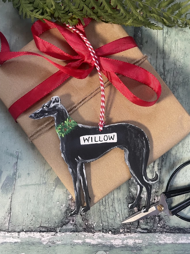 Handpainted black greyhound Christmas ornament placed on a wrapped gift