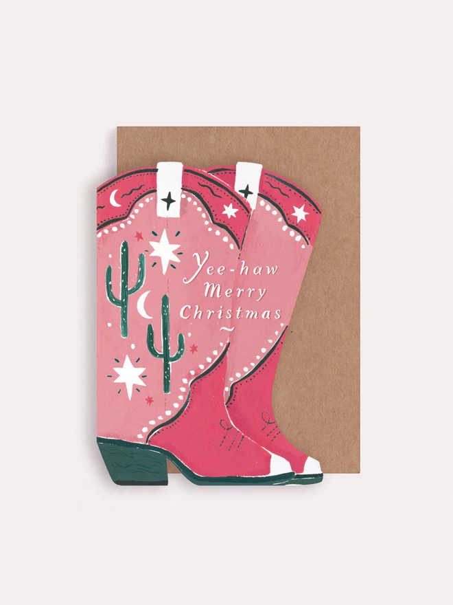 Cowboy Boots Christmas Card, pink cowboy boots illustrated with cactus and stars, beside a kraft envelope