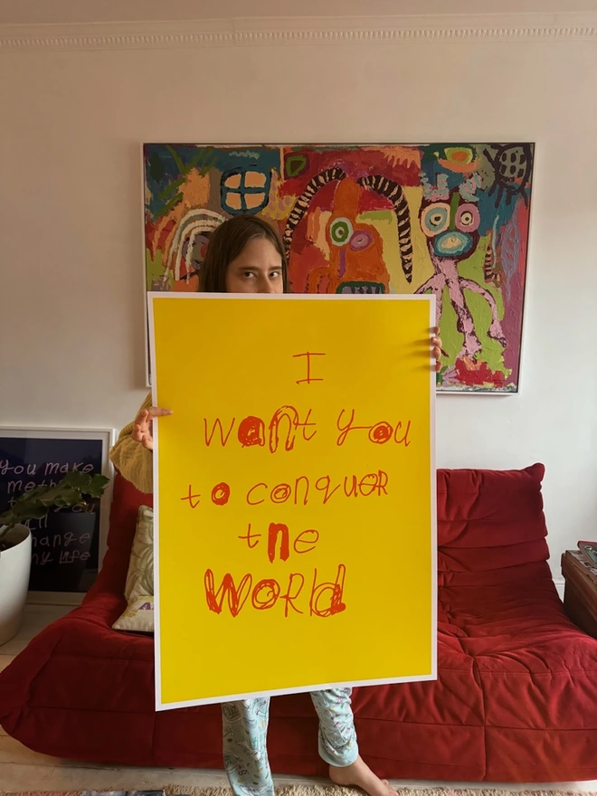 Piper peaking over her screen print that is bright yellow with orange font