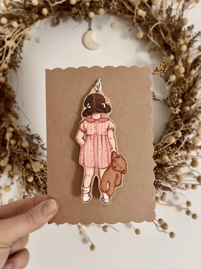 a scalloped kraft card with a diecut swing tag attached of a girl and her teddy