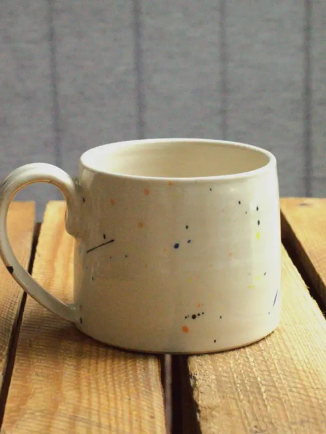 Large creamy white terrazzo cups with black, blue, and yellow splatters and glossy glaze on a wooden surface.